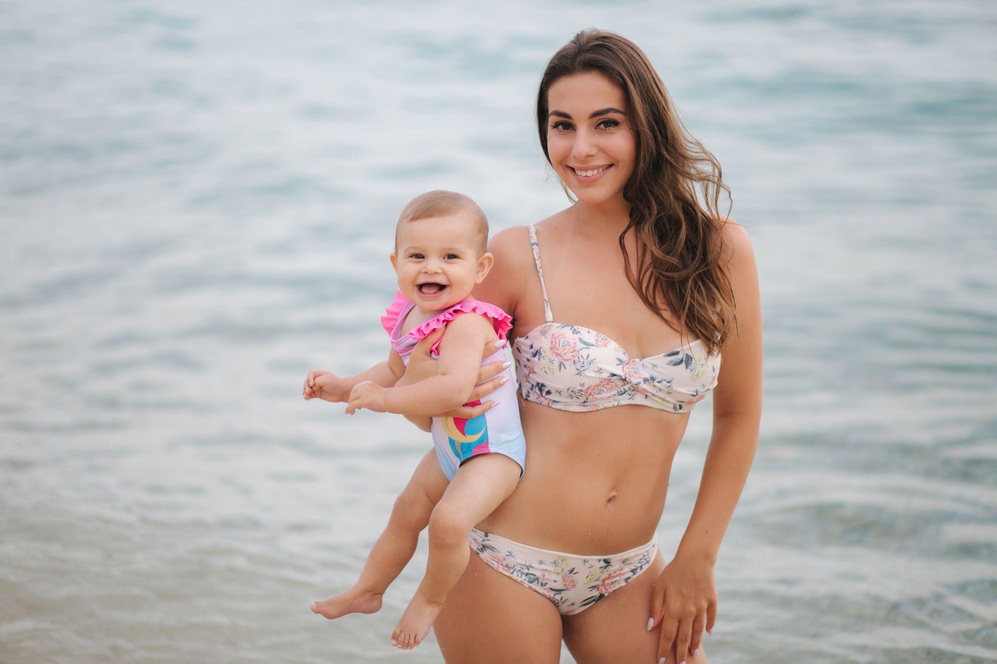 Mom smiling at beach with baby after mommy makeover procedure